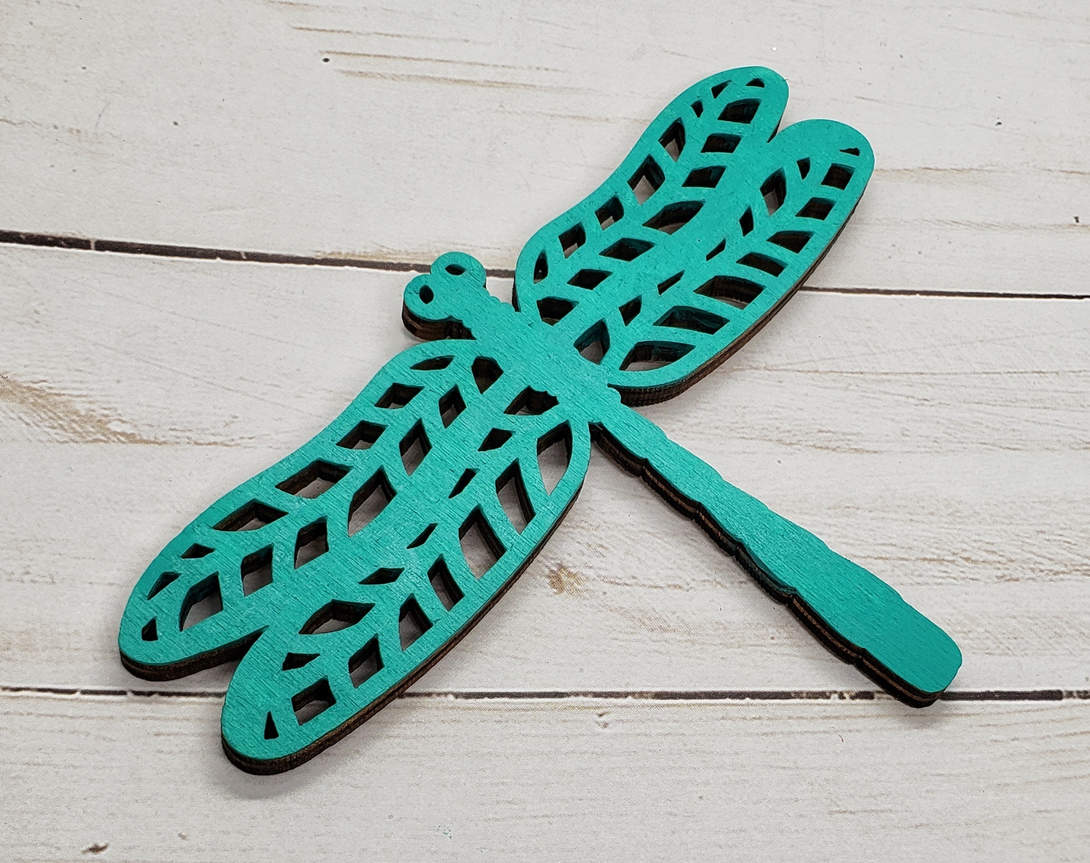 A bright Aqua painted wooden dragonfly on a faux wood background.