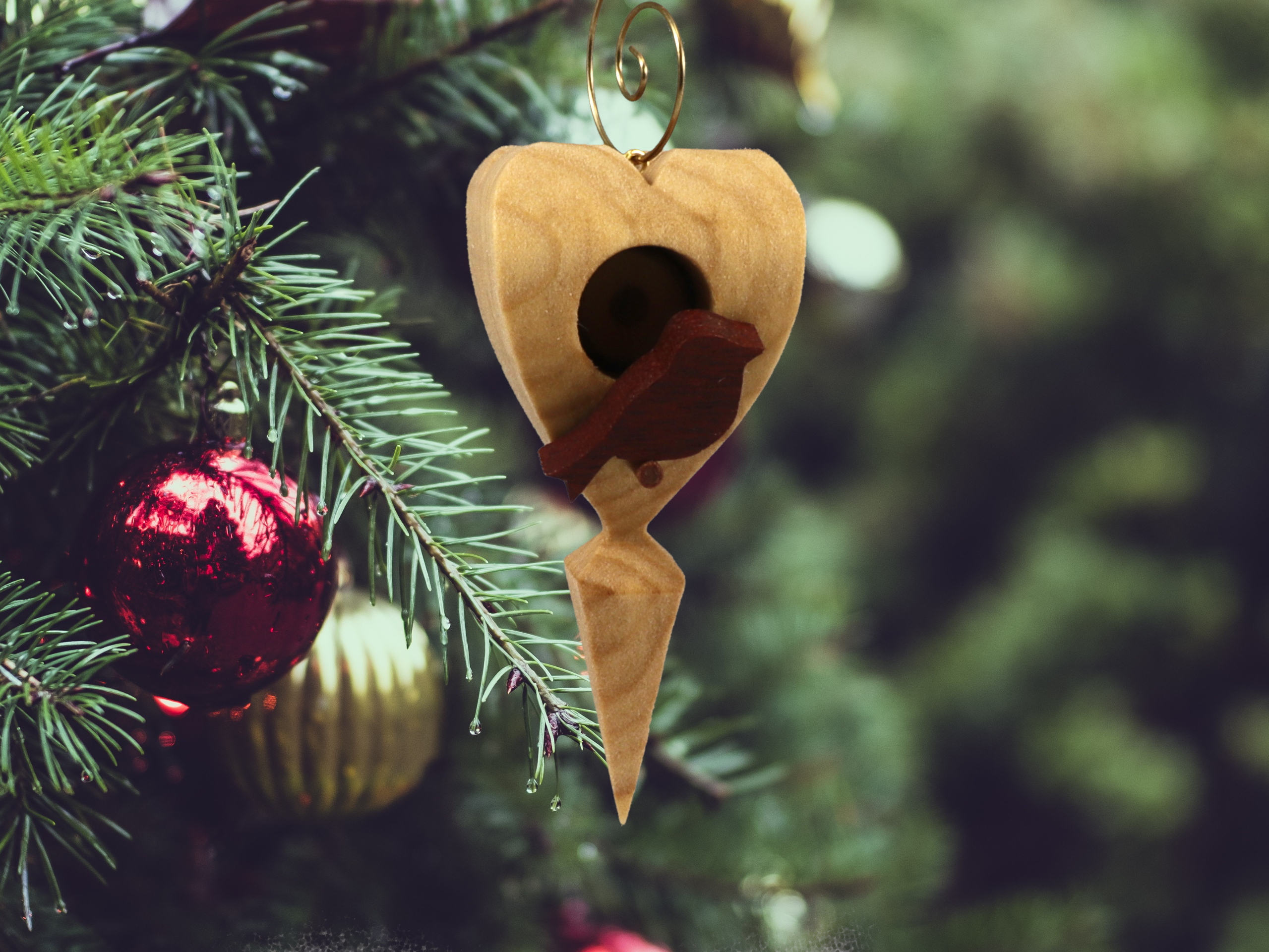 The wooden miniature Birdhouse Ornament is shaped like a heart. A small, dark-reddish-brown bird is perched on the front of the birdhouse. The heart-shaped structure has a pointed bottom that tapers down to a fine point. The wood is light beige.