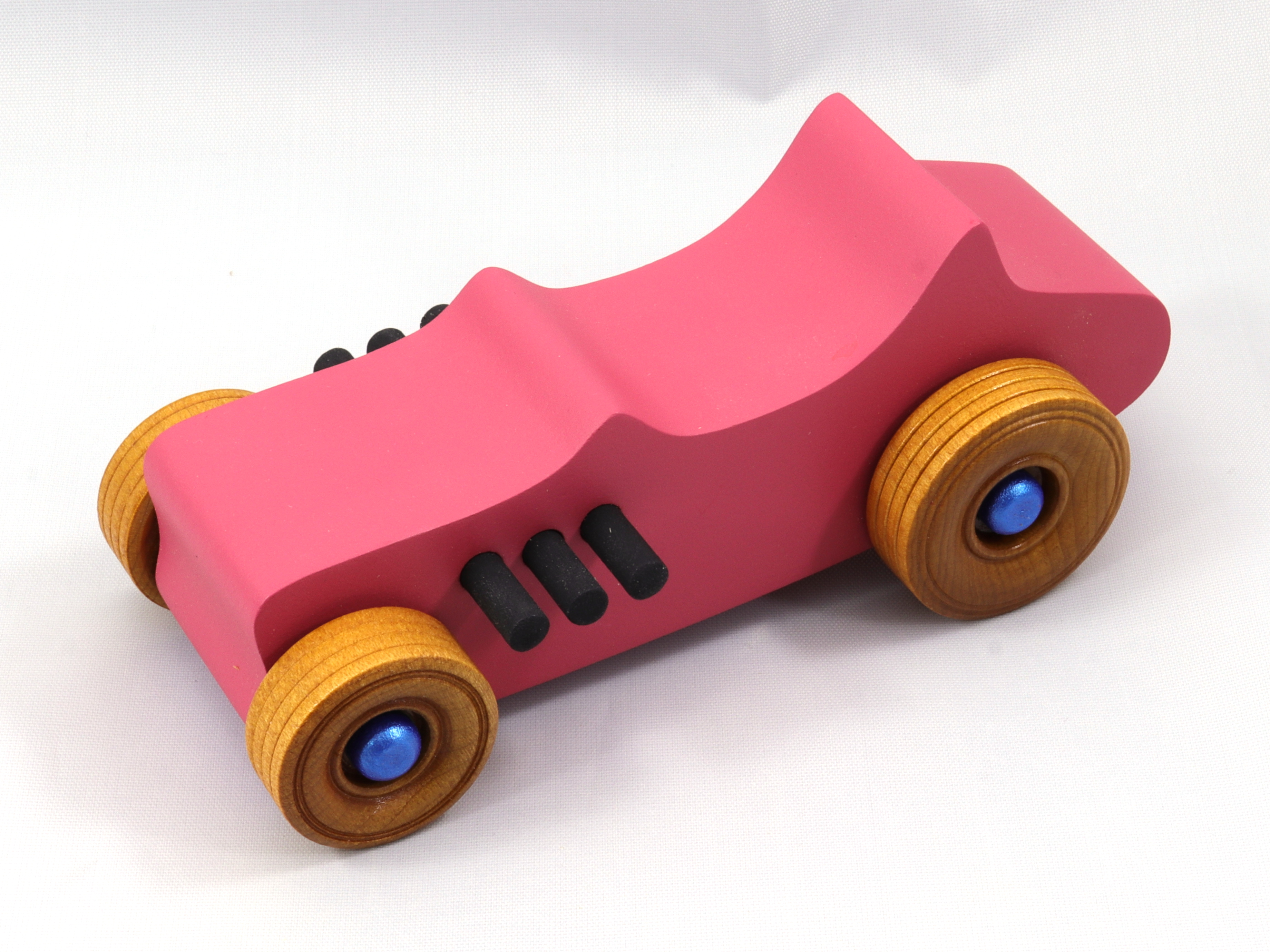 A handmade wood toy 1927 T-bucket Hot Rod car painted with Hot Pink, Metallic Sapphire Blue, and Black Acrylic paint with the wheels finished with nonmarring Amber Shellac.