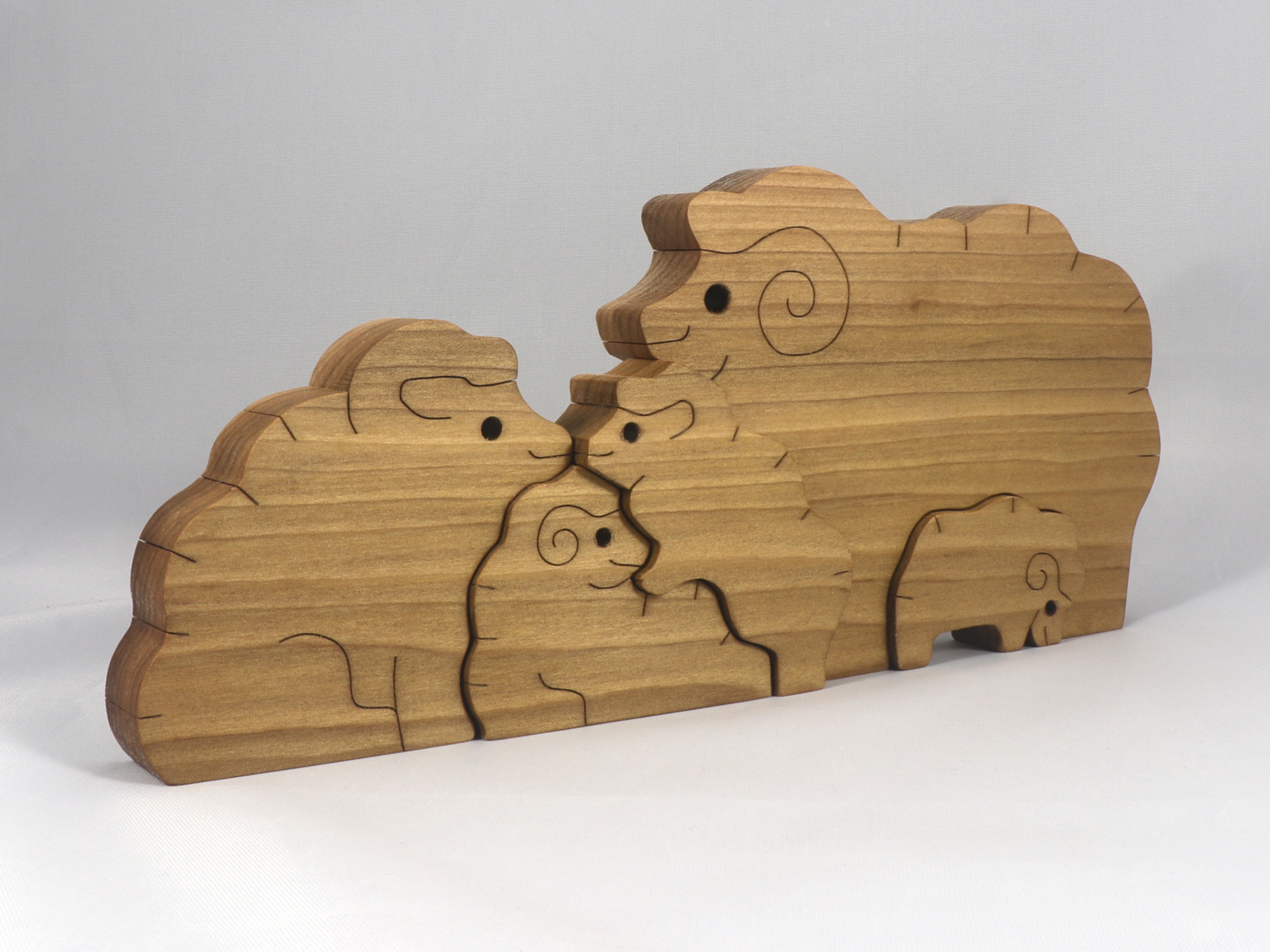 A handcrafted wood sheep family stacking puzzle features a ram, ewe,  and three lambs, all hand-finished with a blend of oils and waxes. The sheep can be used separately for pretend toys.