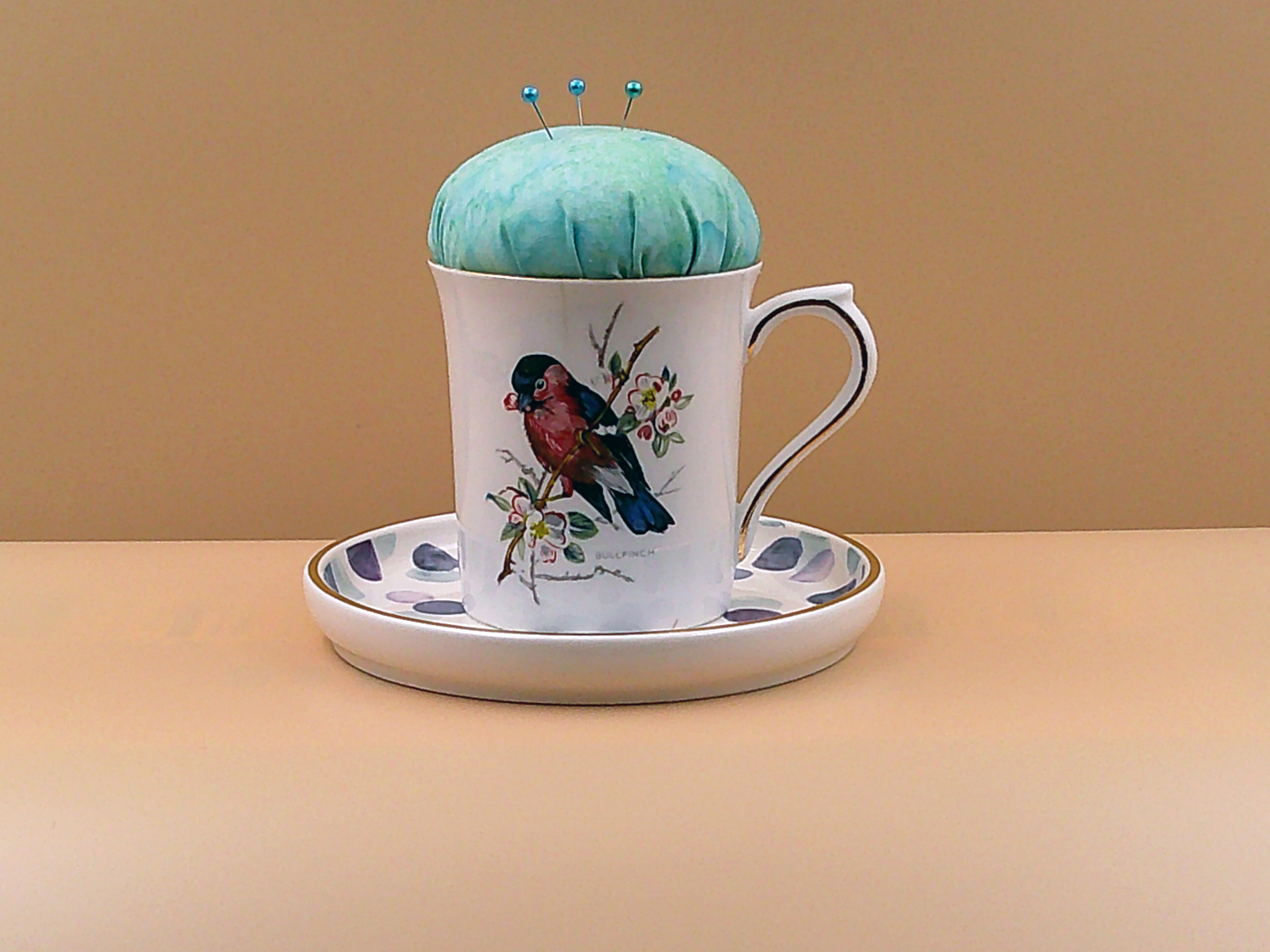 This teacup has a pincushion on the top with some pins and a saucer on the bottom to hold bobbins and other things. It is all one piece. This teacup has a pincushion on the top with some pins and a saucer on the bottom to hold bobbins and other things. It is all one piece.