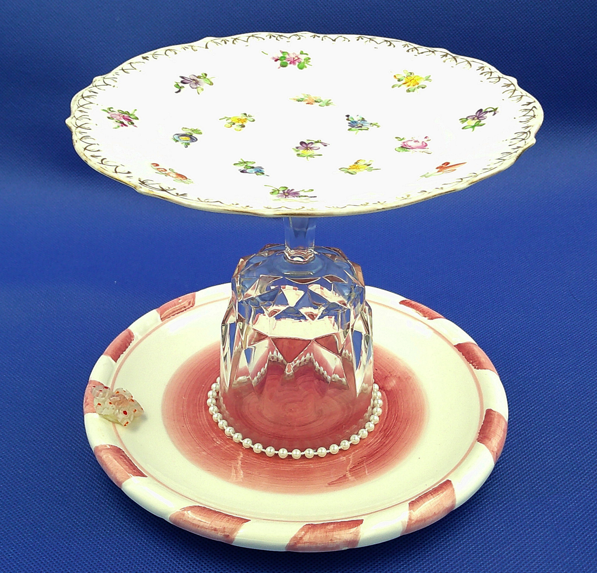 This lollypop jewelry dish has a dark pink and white dish on the bottom with pearls surrounding the crystal goblet. This lollypop jewelry dish has a dark pink and white dish on the bottom with pearls surrounding the crystal goblet.