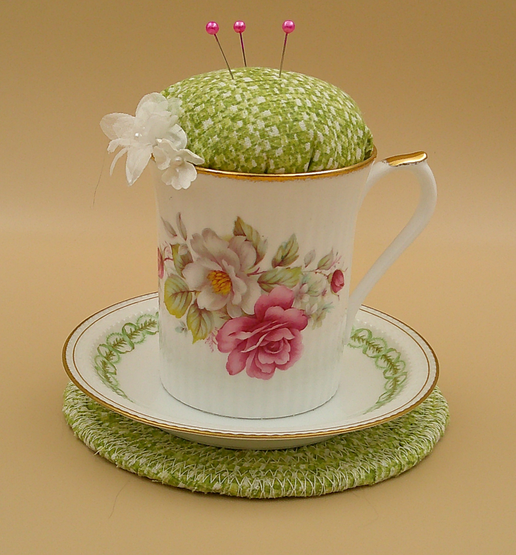 This is a frontal view showing the pincushion bobbin holder sitting on the trivet. The trim on the saucer is complemented by the fabric. This is a frontal view showing the pincushion bobbin holder sitting on the trivet. The trim on the saucer is complemented by the fabric.
