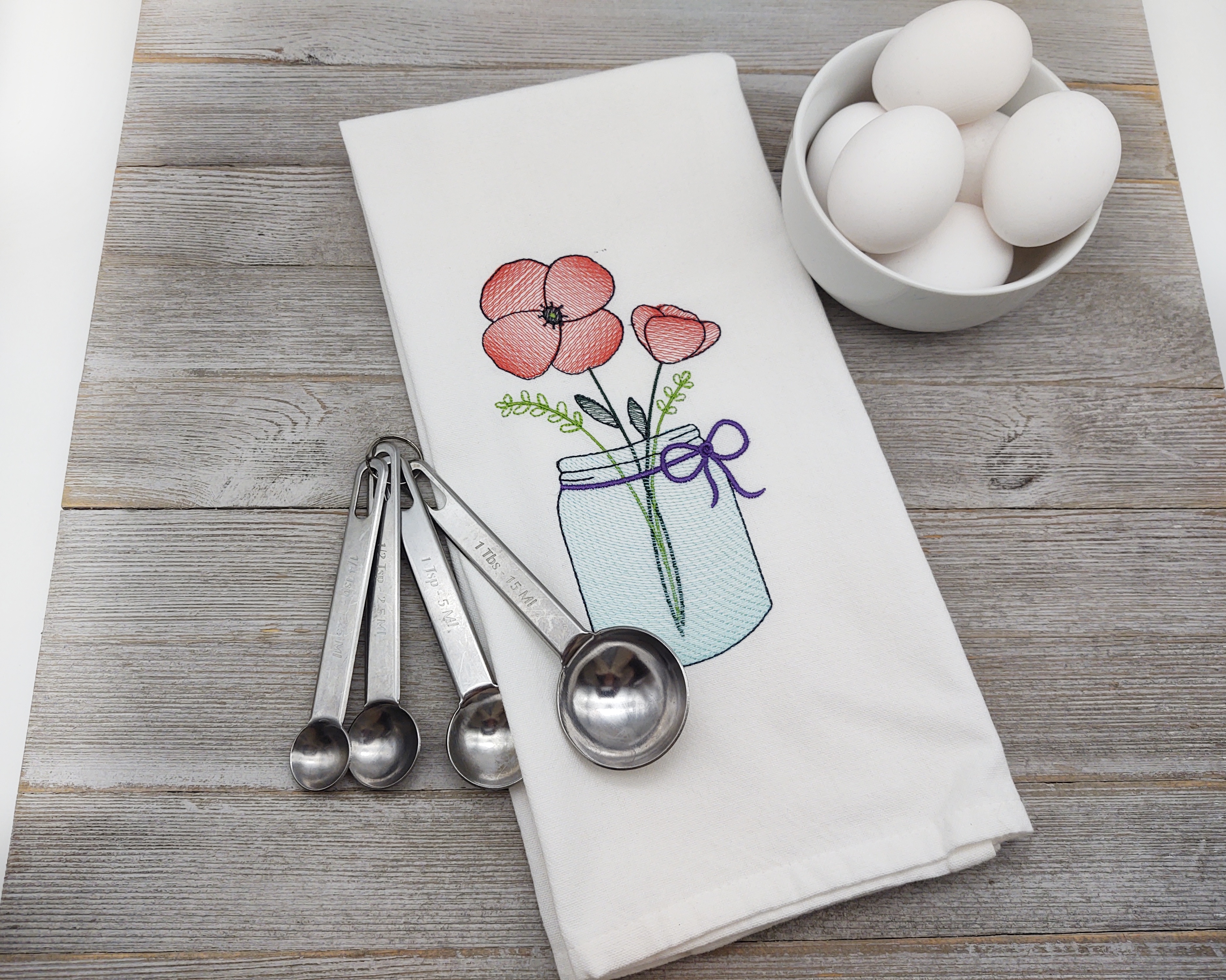 Get rid of the winter blahs or add some cheerful kitchen decor with this blue canning jar with red Poppies on a white cotton tea towel.  Hang it over the the oven handle and show it off.

    What you get:  One white kitchen towel with embroidered red poppies in a blue jar.

    Fabric color:  White flat weave tea towel, red poppies with a sprig of greenery, green leaves and a dark purple bow. 

    Fabrics used:  white flat weave kitchen towel, tear away stabilizer and polyester machine embroidery thread.

    Size:  Dish towel measures 17.5 x 26 inches.  It has a hanging loop on the back side so it can be hung from a hook. Dish towel has been preshrunk.

    Care:  Hand-machine wash in cold water with like colors.  Air dry or dry in dryer.  Press with warm iron on wrong side if necessary.  No bleach.
    List is for hand towel only.  Additional items in pictures are not included.

**NOTE:  all towels I have in my shop are meant to be decorative and are NOT meant for heavy duty use.  They can withstand light daily use, and machine washing.